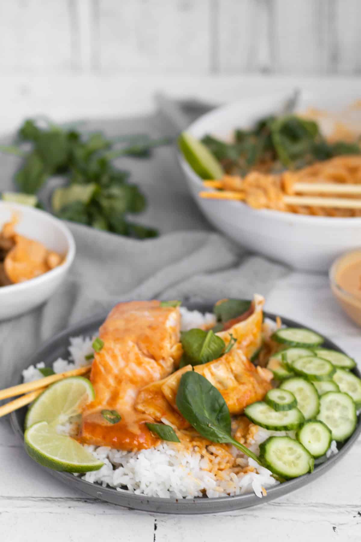 salmon on a plate with rice, cucumbers and curry noodles in the background.