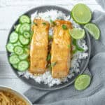 Thai red curry salmon on a bed of rice with limes and cucumbers.