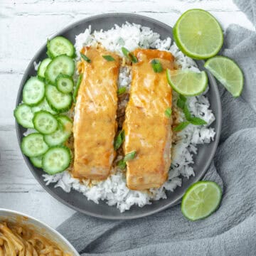 Thai red curry salmon on a bed of rice with limes and cucumbers.
