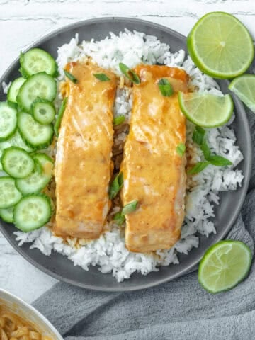 Thai red curry salmon on a bed of rice with limes and cucumbers.