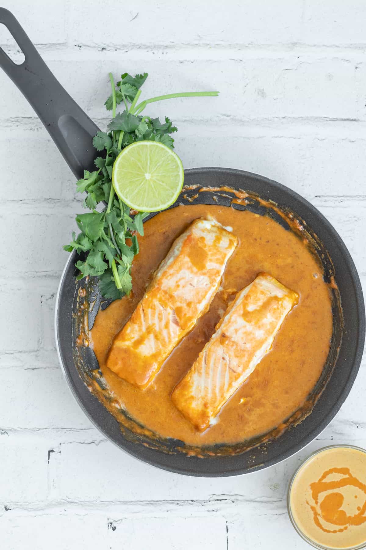 Salmon in a frying pan with sauce a lime garnish.