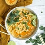 thai red curry noodles in a white bowl garnished with limes.