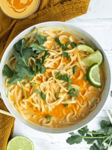thai red curry noodles in a white bowl garnished with limes.